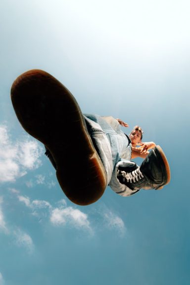 Person mit Blick nach oben, große Schuhe im Vordergrund, blauer Himmel im Hintergrund.